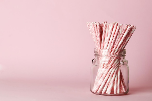 A lot of pink paper straws in a large bottle on a pink background. Top view. Place for text. Party concept.