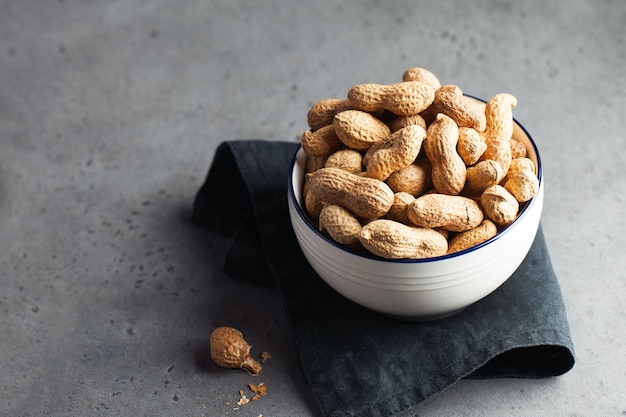 A lot of roasted peanuts in shell in a bowl on a gray surface