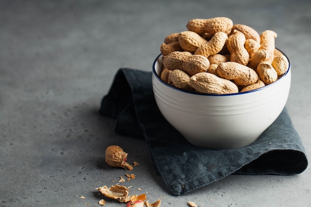 A lot of roasted peanuts in shell in a bowl on a gray surface