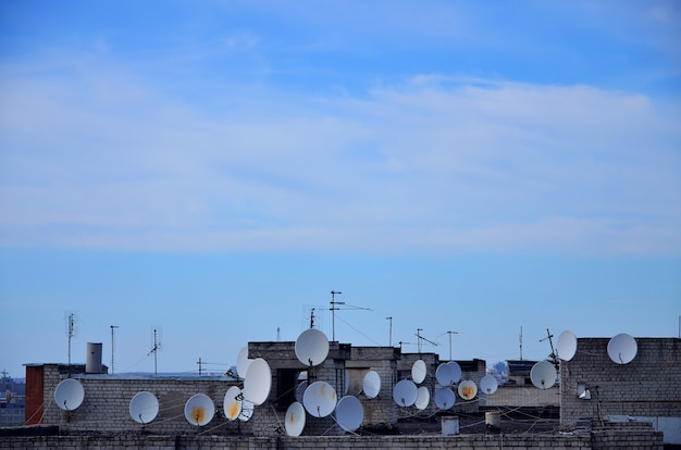 A lot of satellite television antennas on the rooftop under a blue sky