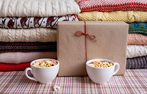 A Lot of Sweaters and Pullovers Different Colours folded in two Piles with Gift box and two cups of coffee.