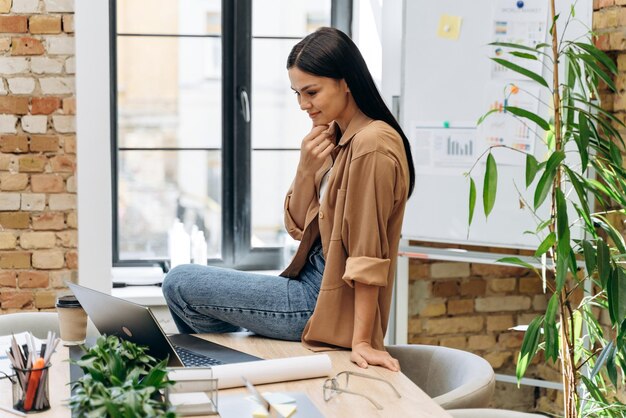 A lot of tasks. Pleasure businesswoman sitting at the table, looking at the laptop screen and thinking about something while working