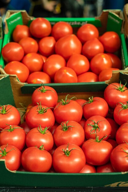 A lot of tomatoes lie on top of each other in the shape of a pyramid in the sunlight