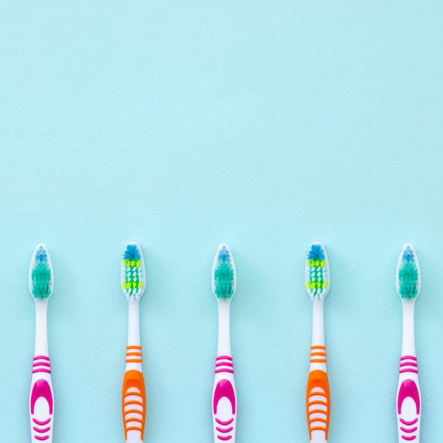 A lot of toothbrushes lie on a pastel blue background. 