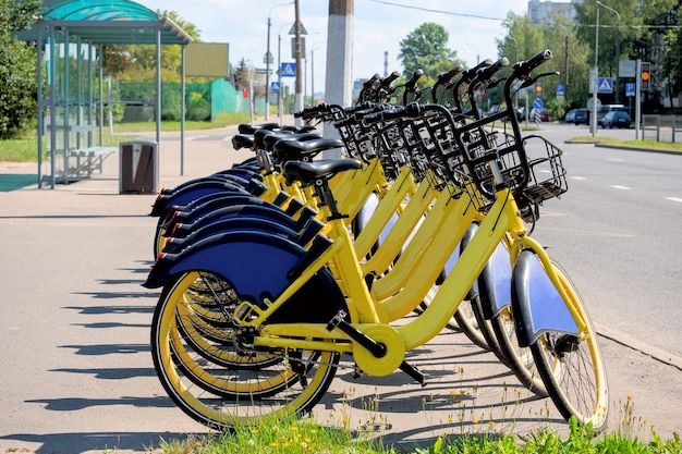 A lot of yellow bikes rental are standing on at a public transport stop