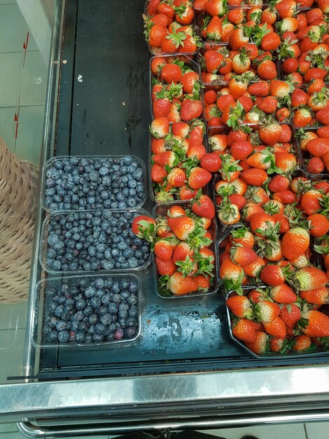 Un sacco di mirtilli e fragole in contenitori sul bancone nel negozio closeup verticale