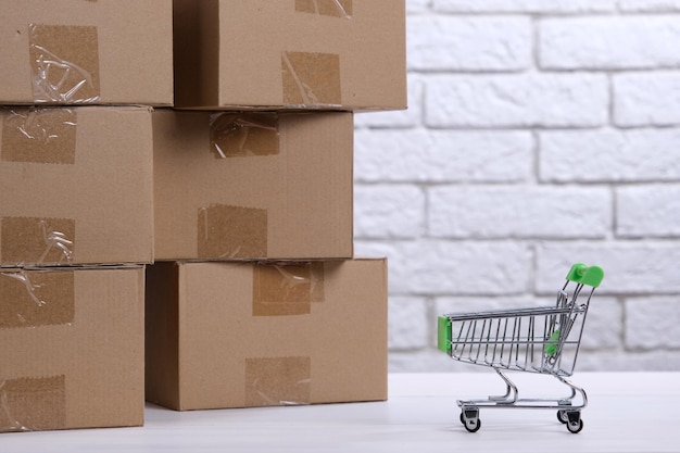 Photo lots of cardboard boxes on the table and a mini shopping cart the concept of ordering goods through online