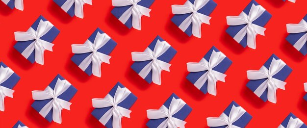 Lots of Christmas gift boxes blue with a white ribbon on a red background. Top view, flat lay. Banner.