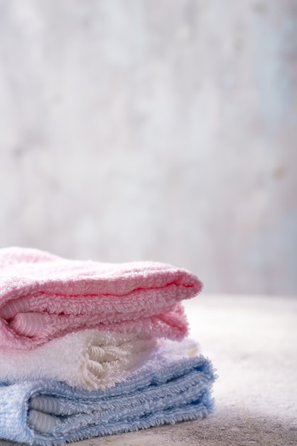 Molti asciugamani di bagno variopinti impilati su a vicenda sulla pietra leggera, copyspace