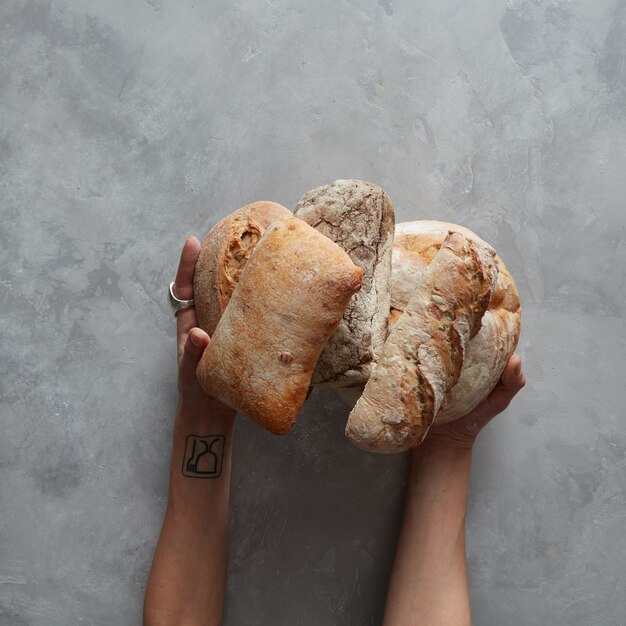 Foto un sacco di diversi tipi di pane nelle mani di un fornaio su uno sfondo grigio, sfondo del concetto di cottura e cottura.