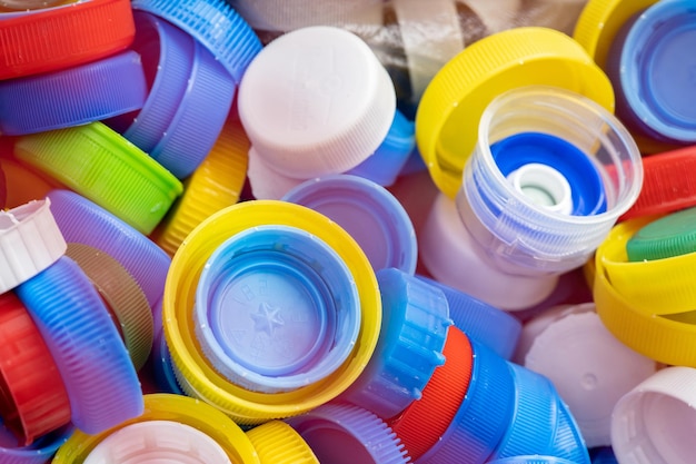 Photo lots of different colored plastic drink bottle caps in a designated recycling container throwing away and collecting bottle caps for charity simple concept nobody macro detail closeup eco lifestyle