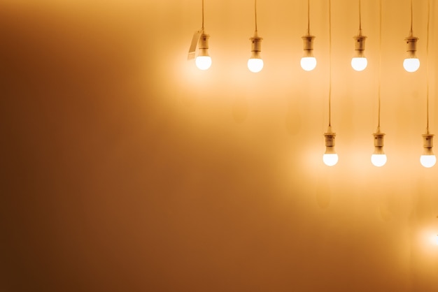 Lots of glowing bulbs hanging in a row against a yellow wall copy space Minimalistic illuminated