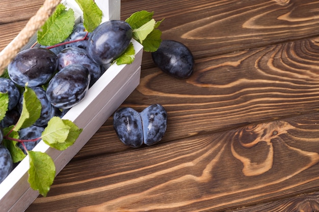 Lots of ripe juicy plums in a white box on the wooden table.