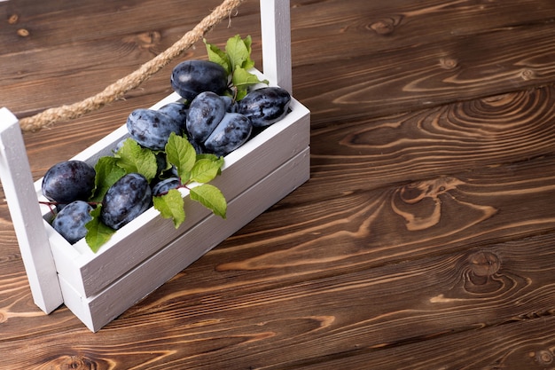 Lots of ripe juicy plums in a white box on the wooden table.