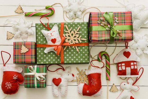 Un sacco di piccole e grandi scatole regalo su uno sfondo di legno. regali in carta colorata decorata con fiocchi di nastro rosso e fiocchi di neve, caramelle. tavola delle feste di natale e capodanno.