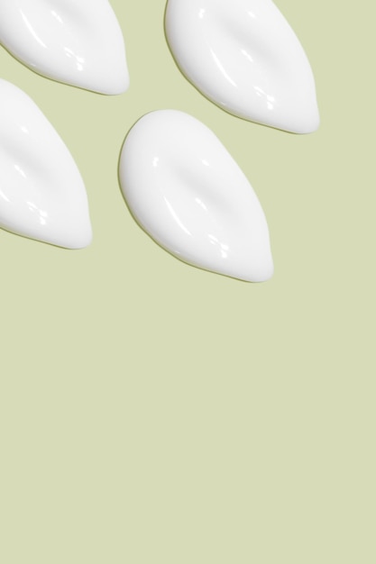 Lots of smears of cosmetic cream Light smooth surface In a row At an angle Top view Texture of flowing cream Liquid creamy strokes On green background Cosmetic background banner