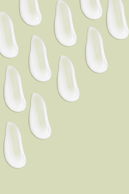 Lots of smears of cosmetic cream Light smooth surface In a row At an angle Top view Texture of flowing cream Liquid creamy strokes On green background Cosmetic background banner