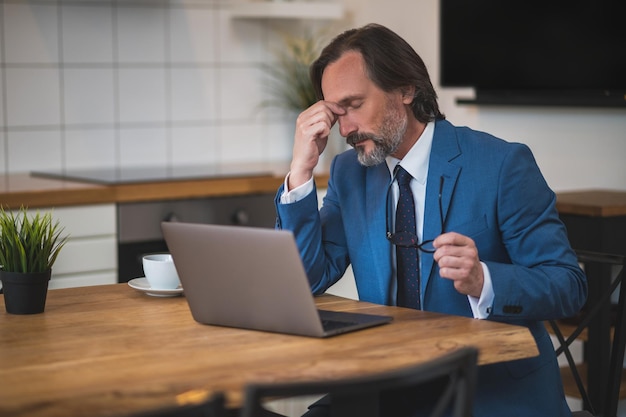 Lots of work. Mature businessman sitting at the laptop and looking tired