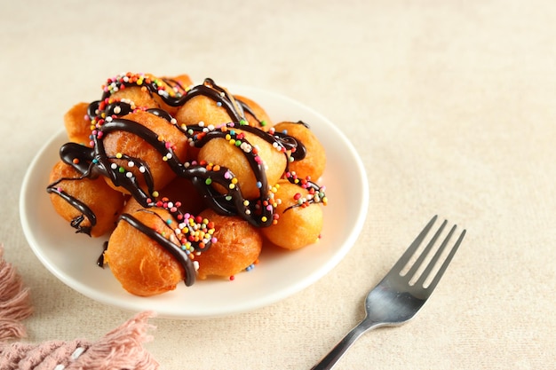 Loukoumades, luqaimat or lokma with chocolate topping with colorful sprinkle in a white plate