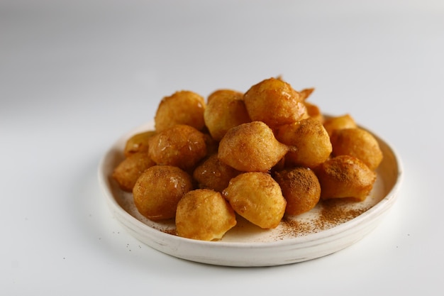 흰색 배경이 있는 접시에 꿀 소스를 곁들인 Loukoumades luqaimat 또는 lokma