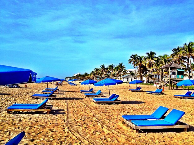 Lounge chairs on beach against blue sky