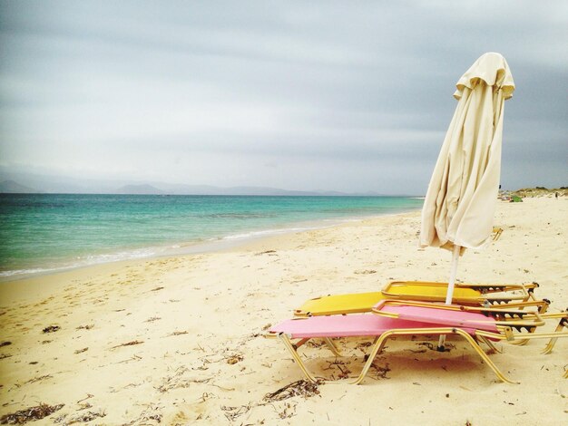 Foto sedie a sdraio e ombrello chiuso sulla spiaggia contro il cielo