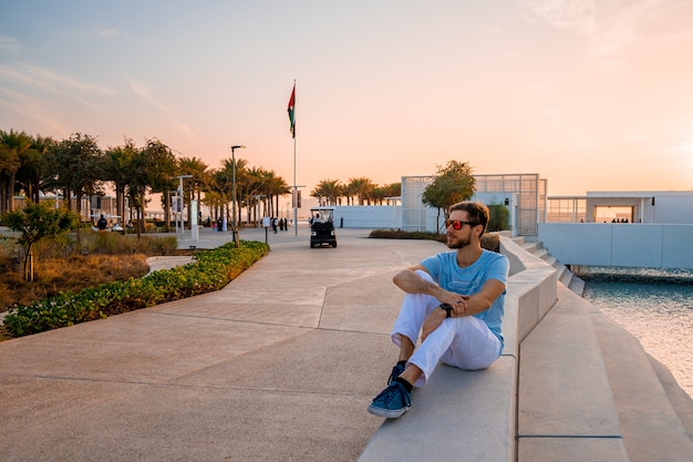 Louvre, Abu Dhabi, Verenigde Arabische Emiraten - 10 mei 2020. Jonge man zit bij het Louvre in Abu Dhabi. Mooi gebouw bij zonsondergang.