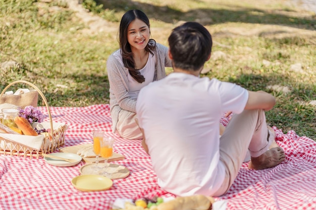 Photo in love asian couple enjoying picnic time in park outdoors picnic happy couple relaxing together with picnic basket