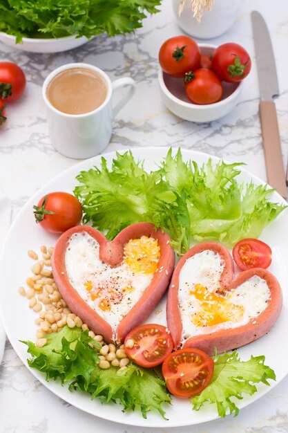 Photo love breakfast fried eggs in heart shaped sausages lettuce and cherry tomatoes on a plate