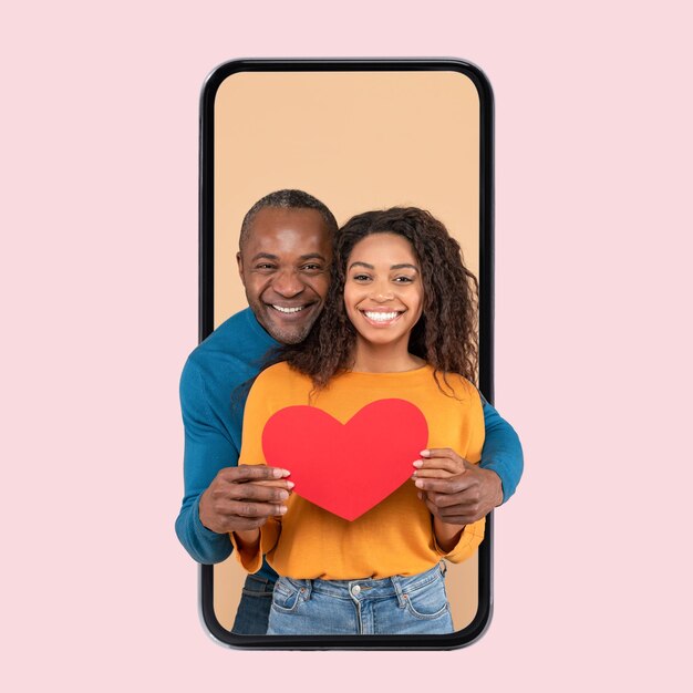 Love and care Happy black spouses hugging holding red paper card heart standing inside cellphone screen