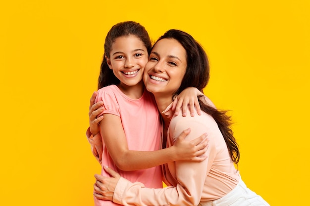 Love and care happy young mother hugging her daughter and smiling at camera expressing tenderness