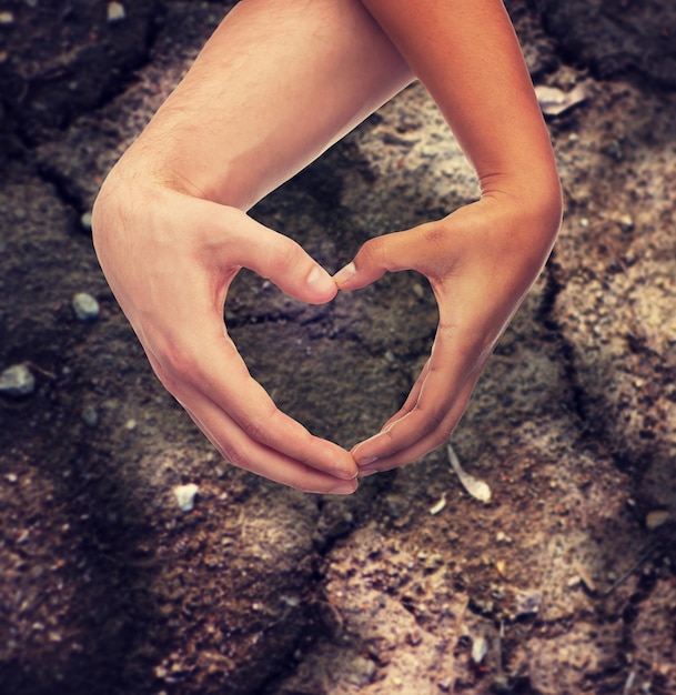 love, care, hope and charity concept - closeup of woman and man hands showing heart shape over ground background