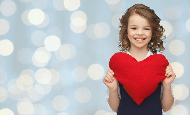 Photo love, charity, holidays, children and people concept - smiling little school girl with red heart over lights background