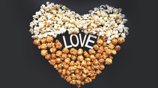 Love Cinema concept of popcorn arranged in a heart shape. Assorted popcorn set background. Sweet and salty popcorn on black background.