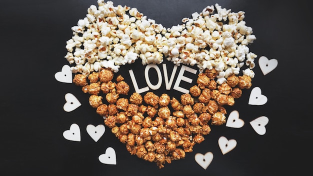 Love Cinema concept van popcorn gerangschikt in de vorm van een hart. Geassorteerde popcorn instellen achtergrond. Zoete en zoute popcorn op zwarte achtergrond.