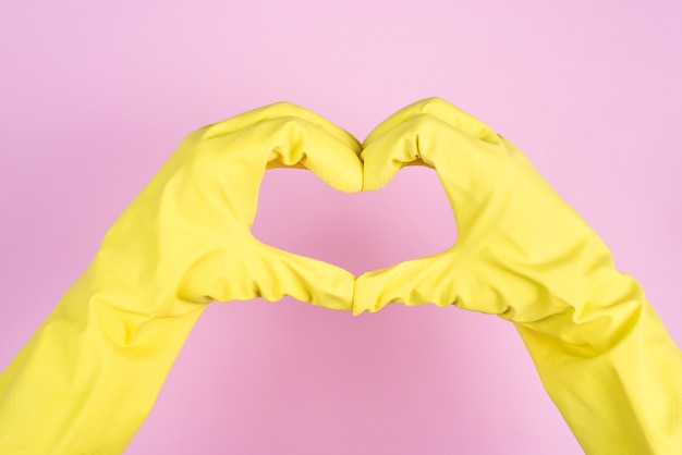 Love cleaning concept. Cropped close up photo of hands is latex gloves making showing heart isolated over pastel background