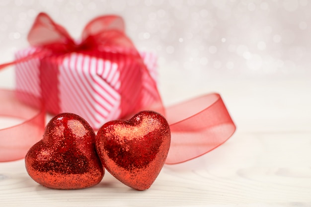 Любовная композиция с двумя красными сердцами и подарочной коробкой на фоне боке