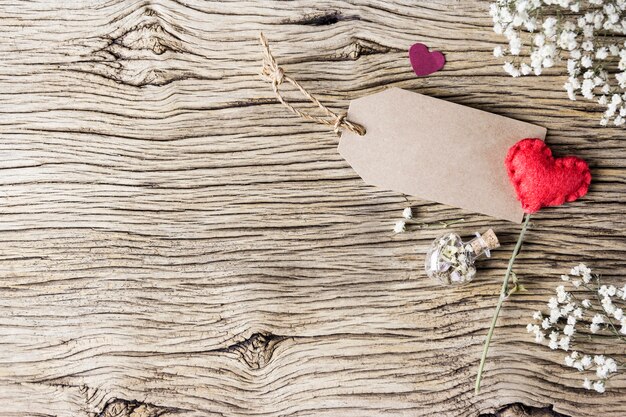 Love concept of blank brown paper tag with red heart and flowers on old wood