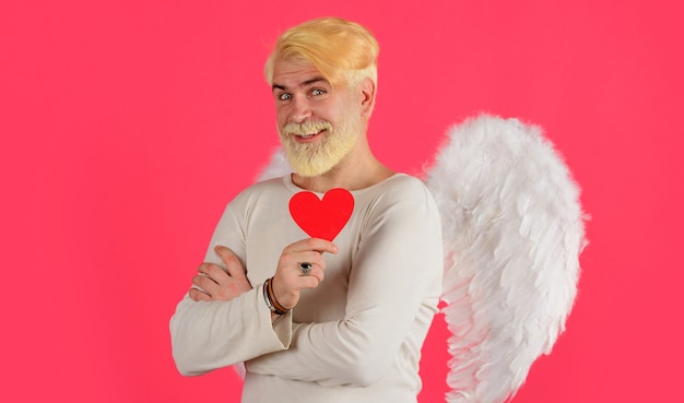 Love concept, handsome angel with red heart, bearded man with\
angel wings, valentines day.