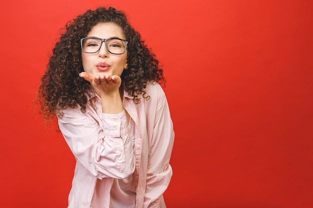 愛の概念。赤の背景に分離されたキスを吹いてポーズ美しいブルネット少女の肖像画。