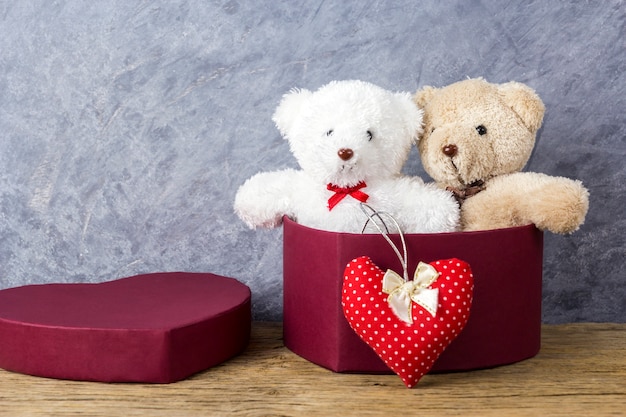 Love concepts of teddy bear in red heart gift box on wood table for valentines day