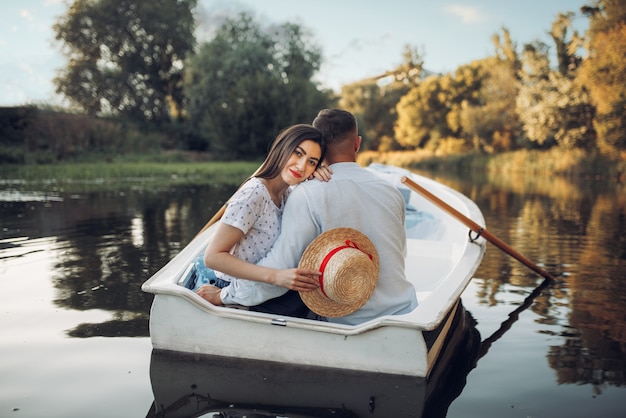 Love couple in boat on quiet lake at summer day. Romantic date, boating trip, man and woman walking along the river