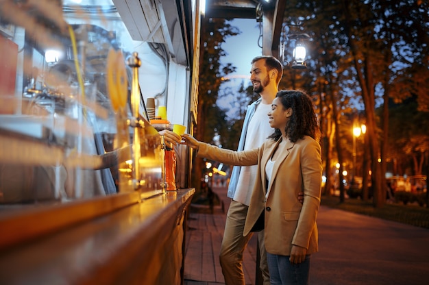 Love couple buying coffee in city amusement park. Man and woman relax outdoors. Family leisures in summertime, entertainment theme