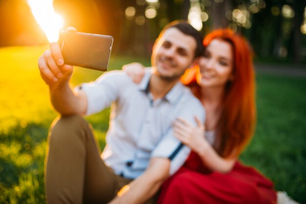 愛のカップルは日没で夏の公園でselfieを作る