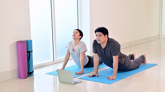 Love couple online learning yoga breathing and meditation together at home. Sport and Exercise for healthy. Asian woman and man lifestyle.