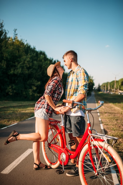 夏の公園、若い男と女のロマンチックなデートを歩いてビンテージ自転車とカップルが大好きです。ボーイフレンドとガールフレンドの屋外、レトロな自転車