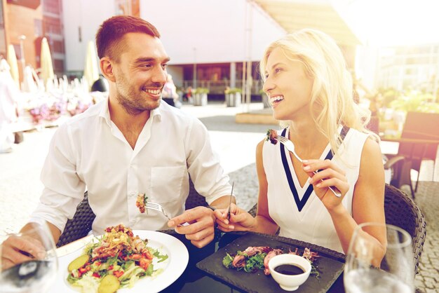 Foto concetto di amore, data, persone, vacanze e relazioni - coppia felice che mangia insalata per cena al bar o alla terrazza del ristorante