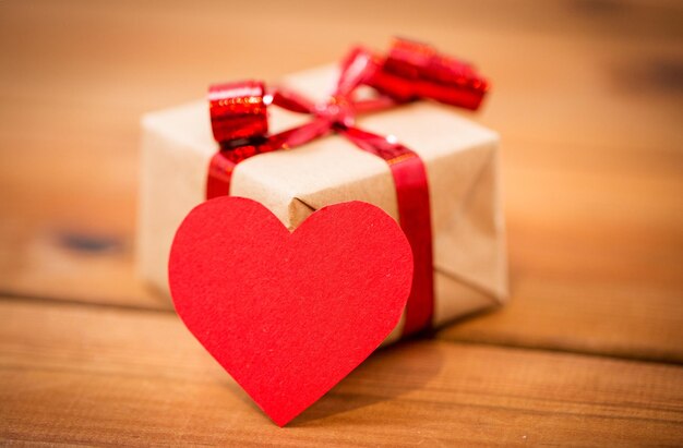 love, date, romance, valentines day and holidays concept - close up of gift box and blank red heart-shaped note on wood