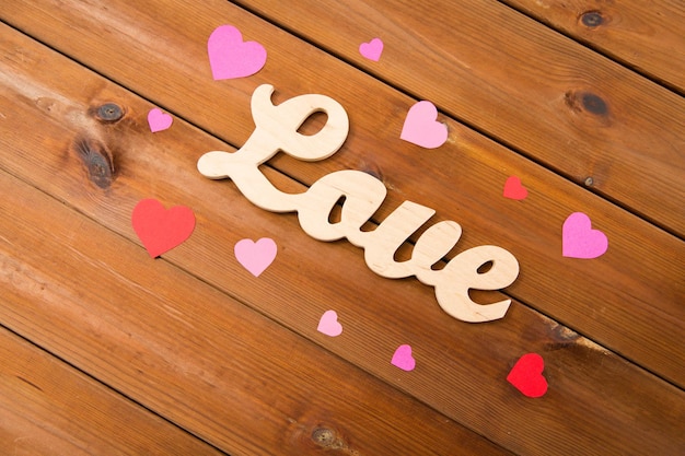 love, date, romance, valentines day and holidays concept - close up of word love with red and pink paper hearts on wood