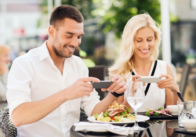 Love, date, technology, people and relations concept - happy couple with smatphone taking picture of food at restaurant